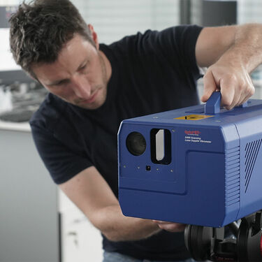 Person aligning a CLASSIC Series laser vibrometer, about shoebox-sized, mounted on feet.