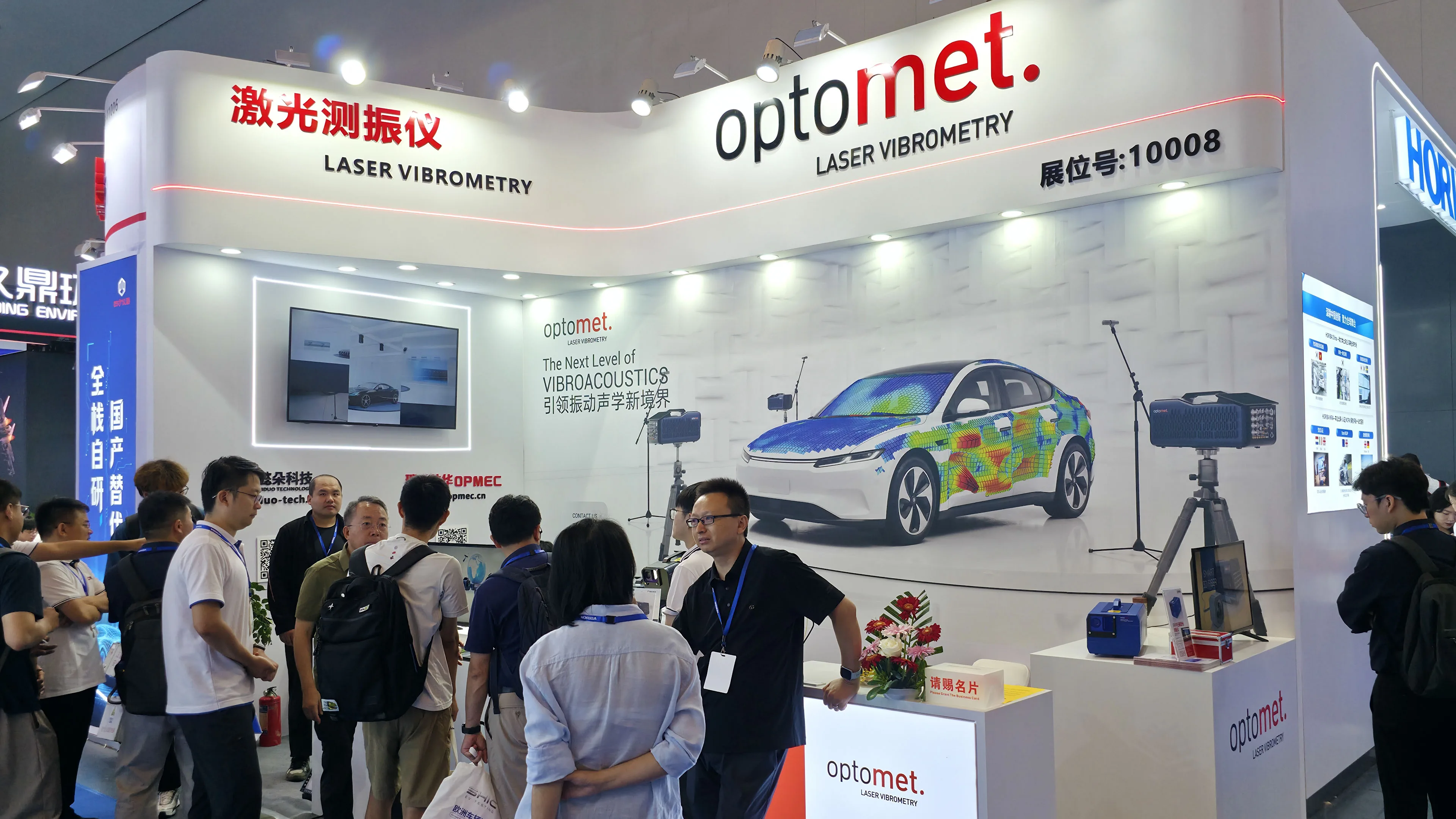 중국 전문 전시회의 레이저 진동 측정용 Optomet 부스: 차량의 색상 코드 진동 분석을 보여주는 벽면 그래픽 앞에 서 있는 방문객들.